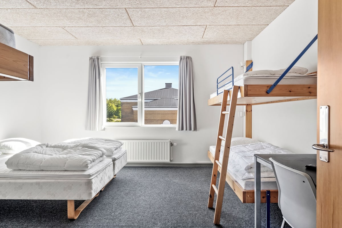 Un dormitorio con literas, un escritorio y una ventana con cortinas.