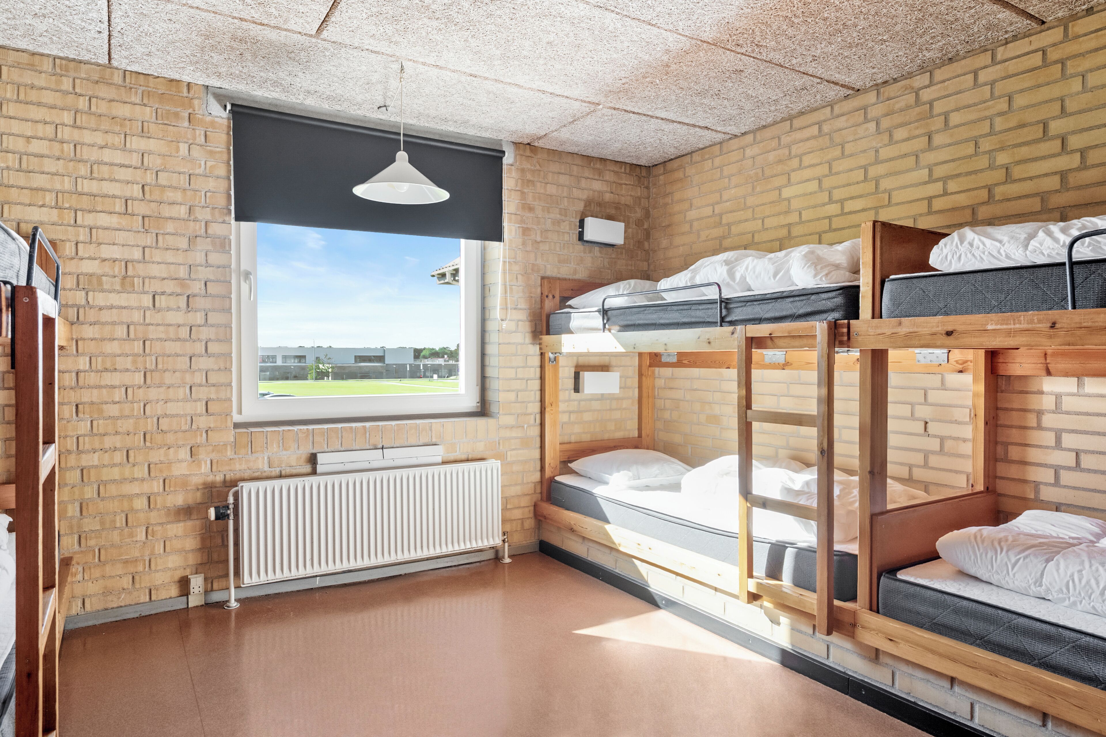 A bunk bed room with a brick wall, a window, and a radiator.