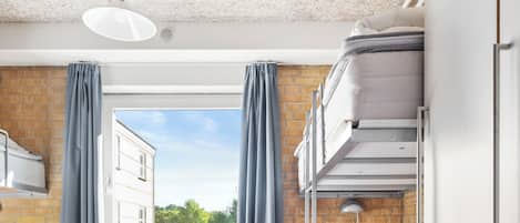 A dormitory room with bunk beds, a table, and a window with curtains.