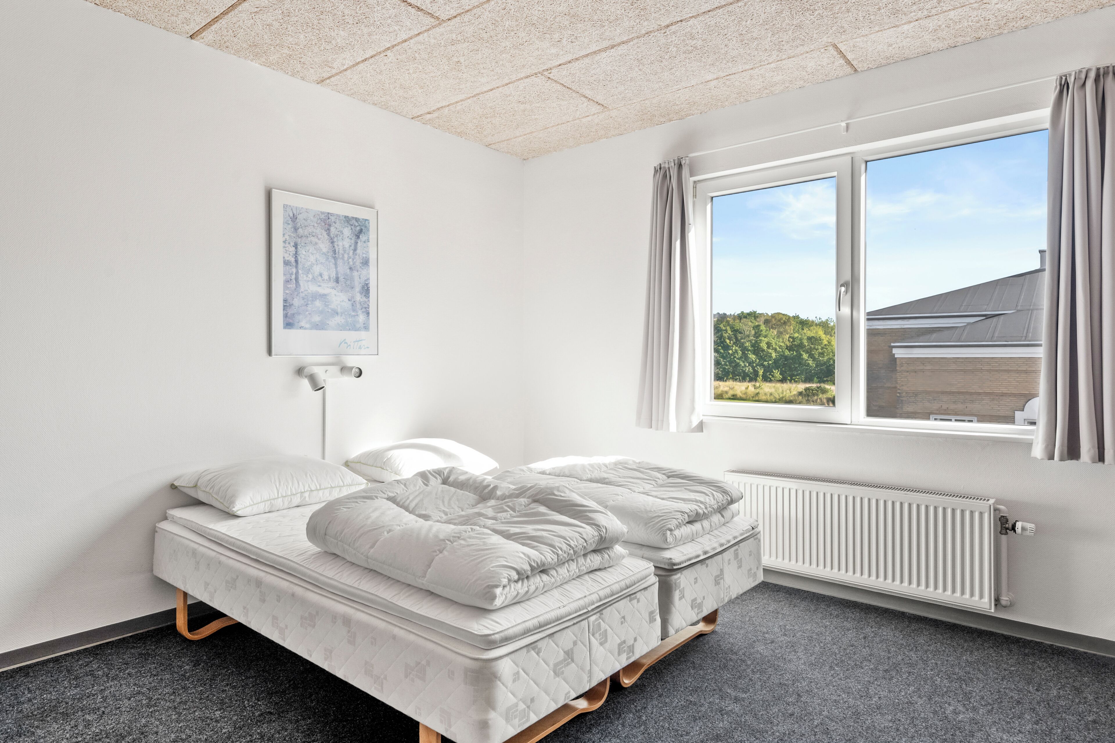 Un dormitorio con dos camas, una ventana con cortinas, un radiador y un cuadro en la pared.