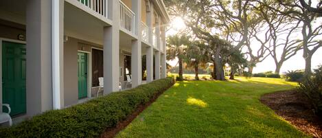 A building with a covered porch, green doors, and a well-maintained lawn.