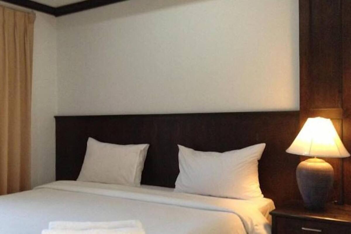 A hotel room with a bed, two pillows, a nightstand with a lamp, and a curtain.