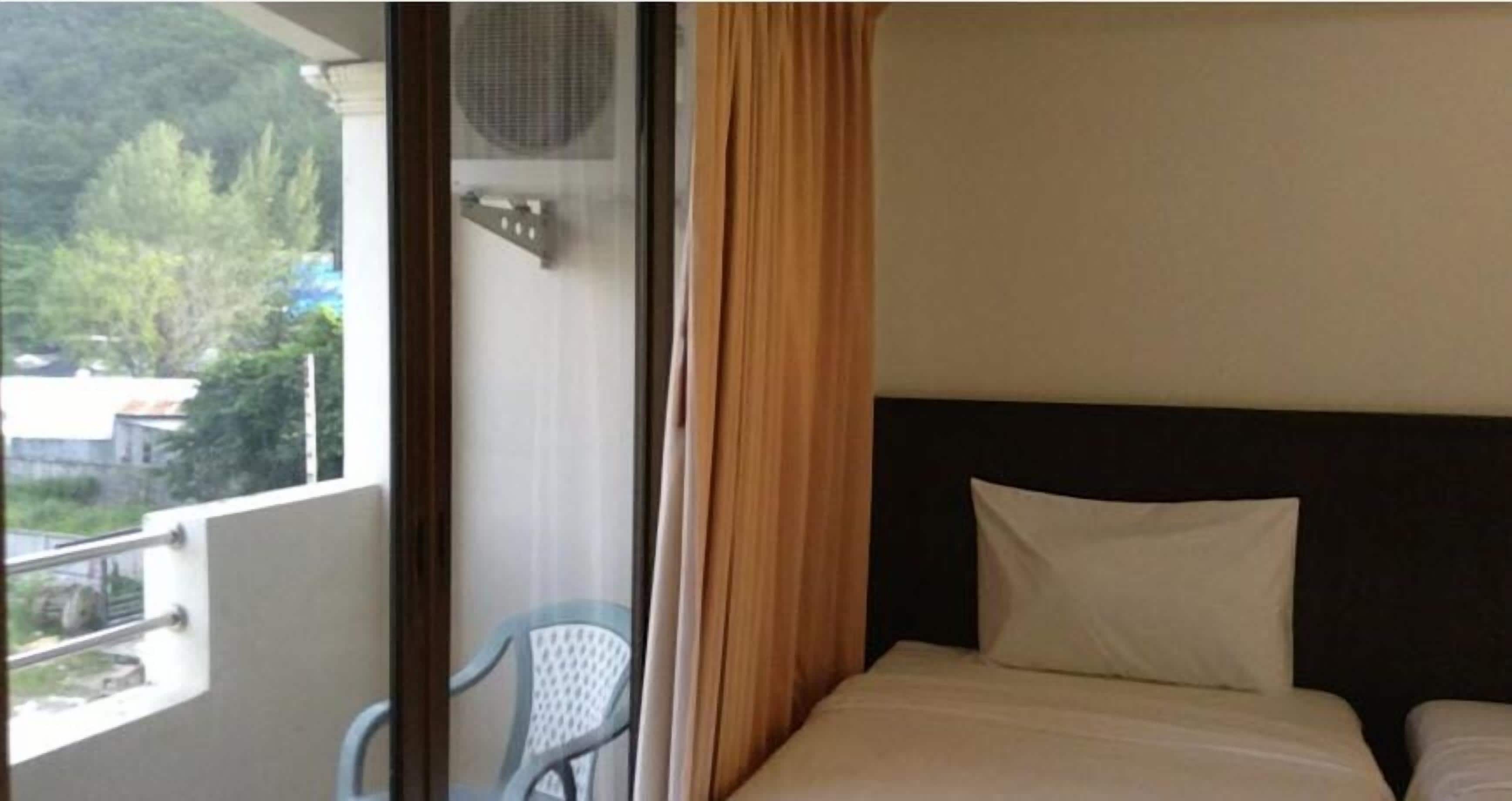 Quarto de hotel com cama, uma cadeira e varanda com vista para árvores e edifícios.