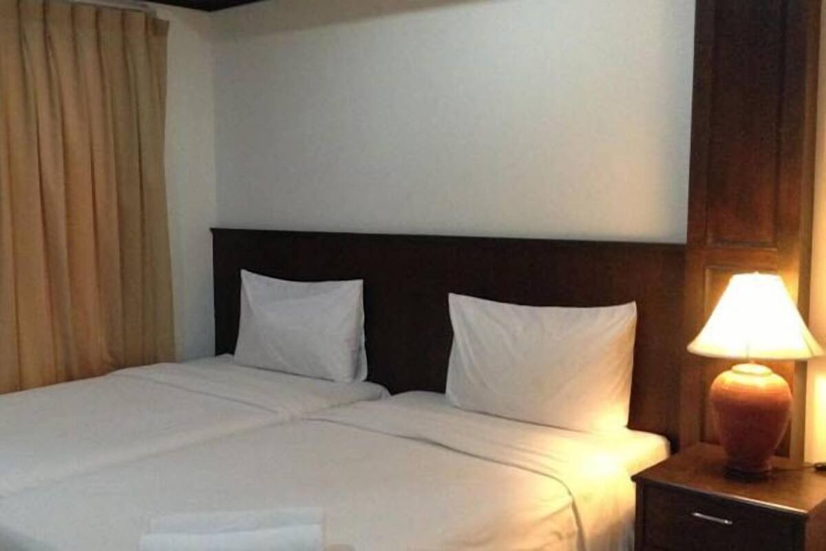 A hotel room with a double bed, a nightstand with a lamp, and a window with curtains.