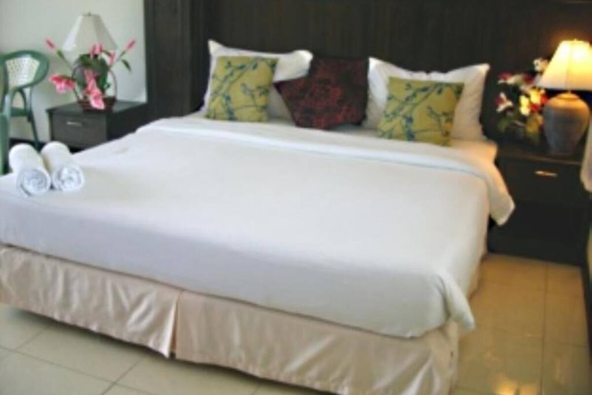 A hotel room with a large bed, a nightstand with a lamp, a chair, and a small table with flowers.