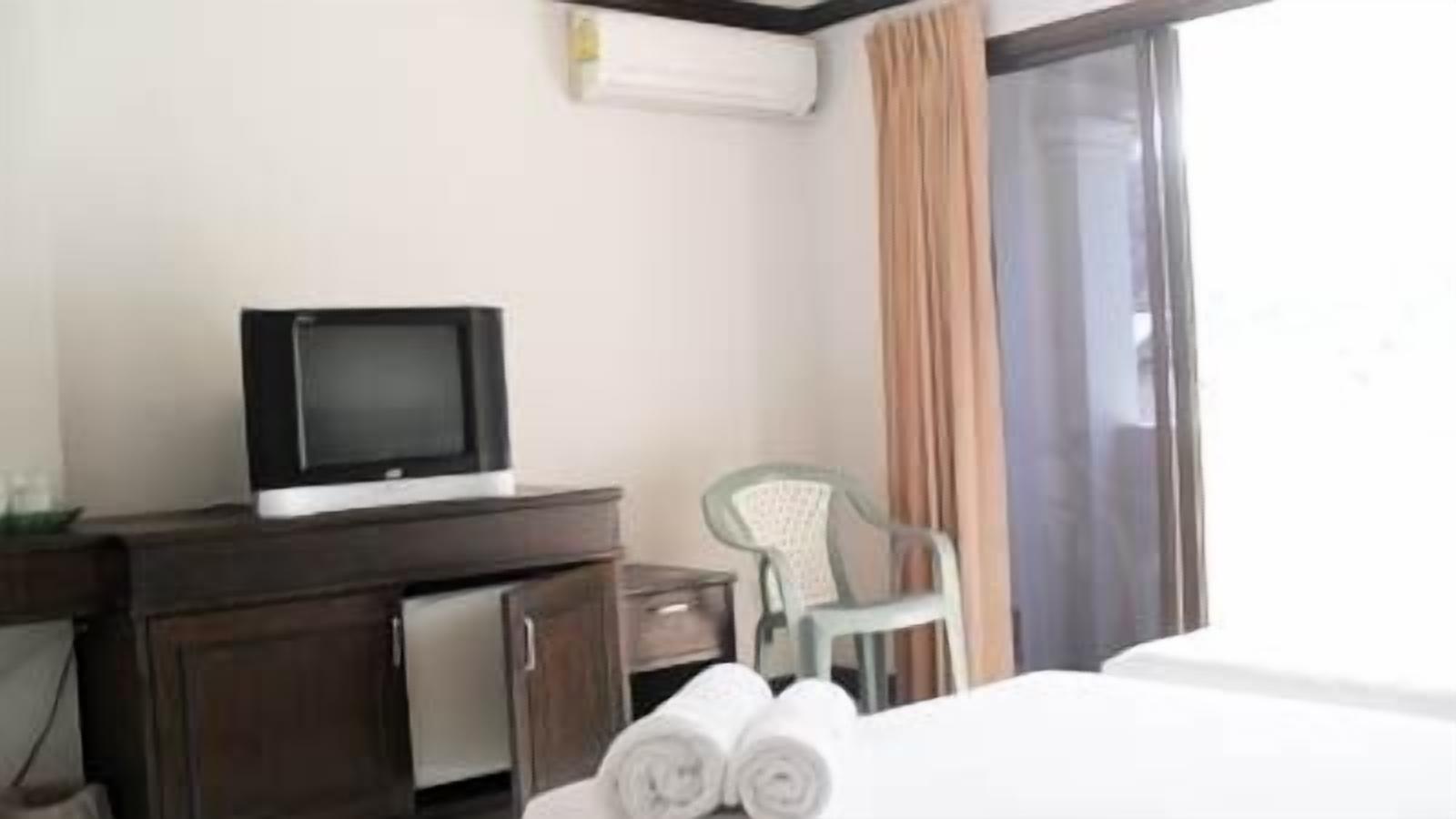 A hotel room with a bed, a desk with a television, a chair, and a window with curtains.