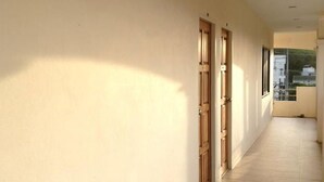 A corridor with beige walls and wooden doors, leading to a balcony with a view of buildings. - Kamala Phuyai Resort (Kamala)