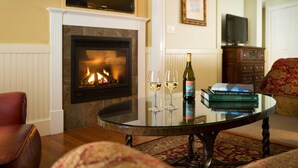 Een woonkamer met een open haard, een glazen tafel met wijnglazen en boeken, en een televisie aan de muur.