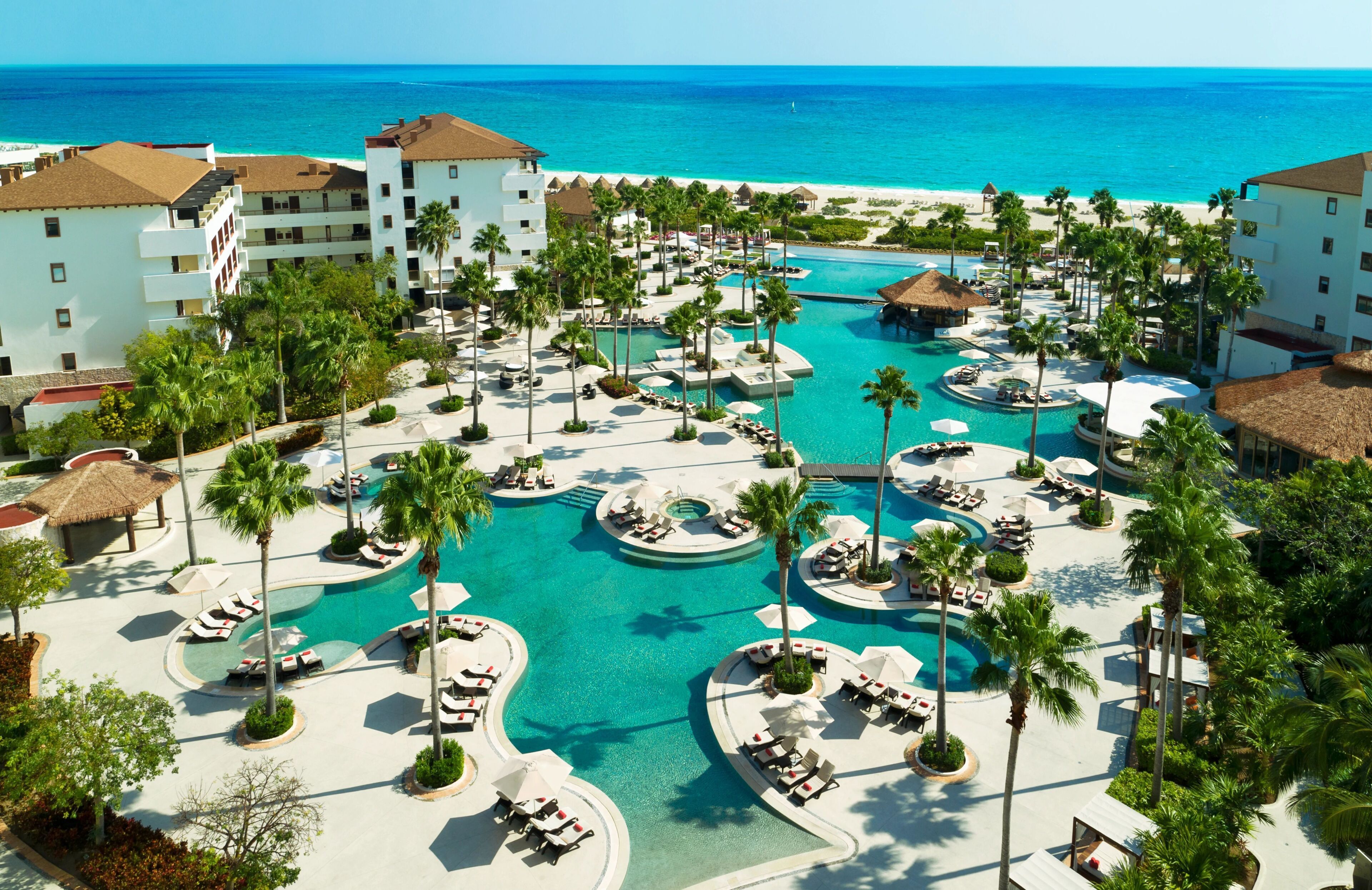 A resort with multiple swimming pools, palm trees, and beachfront views.