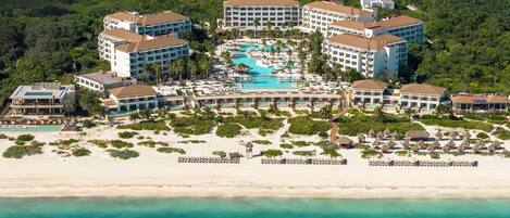 An aerial view of a resort with multiple buildings, a central pool, and a beach.
