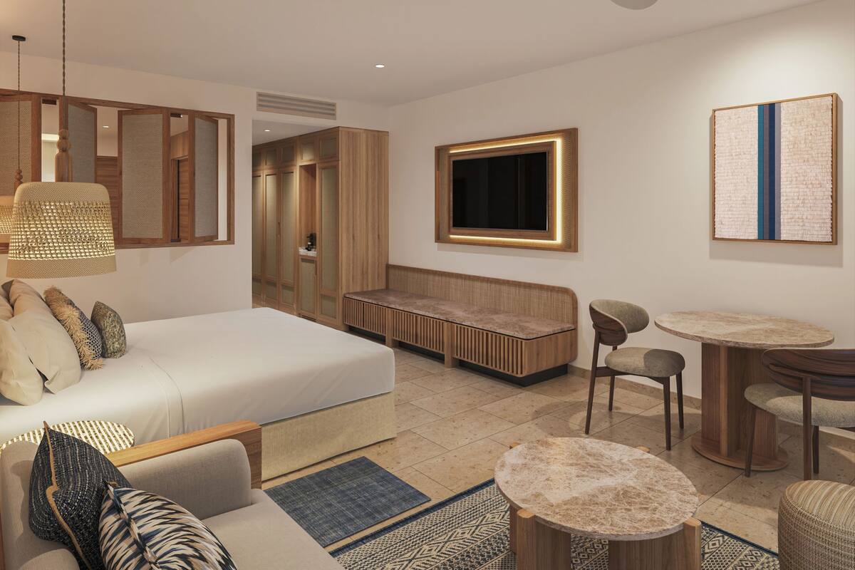 A modern hotel room with a bed, seating area, TV, and a dining table.