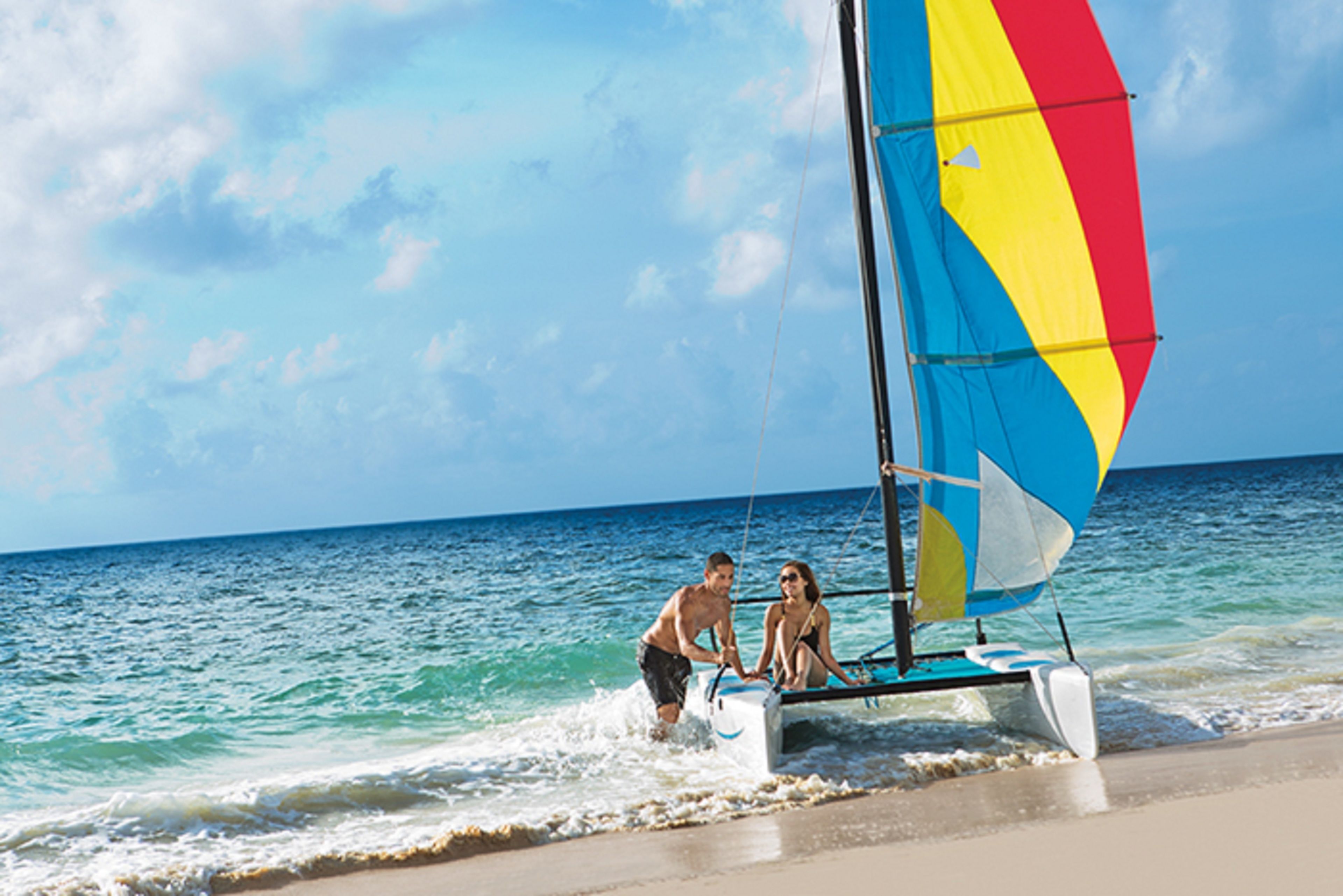 Ein Segelboot mit buntem Segel an einem Strand.
