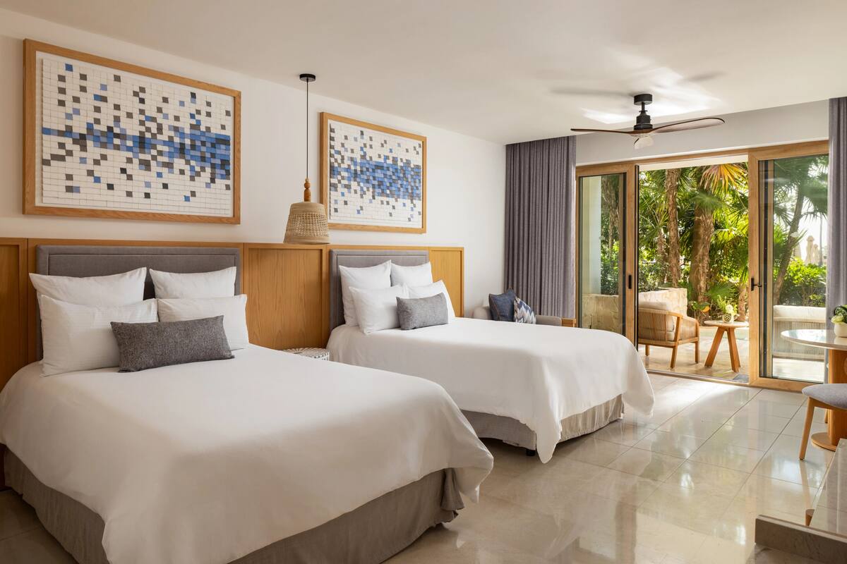 A hotel room with two beds, a ceiling fan, and a view of the outdoors.