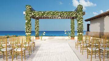 Salón de bodas al aire libre con alfombra blanca, sillas doradas y arcos florales.