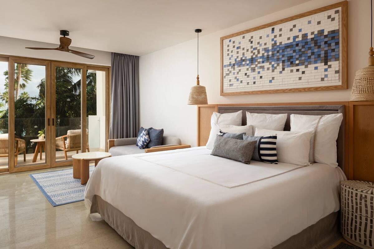 A bedroom with a large bed, a ceiling fan, a view through glass doors, and a woven lamp.