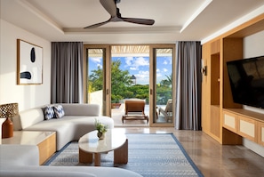 A modern living room with a sofa, coffee table, and TV stand, large sliding glass doors leading to a balcony with outdoor furniture.