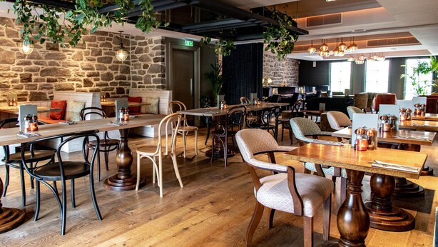 A restaurant with wooden tables and chairs, stone walls, and hanging plants. - The Raeburn (Edinburgh)