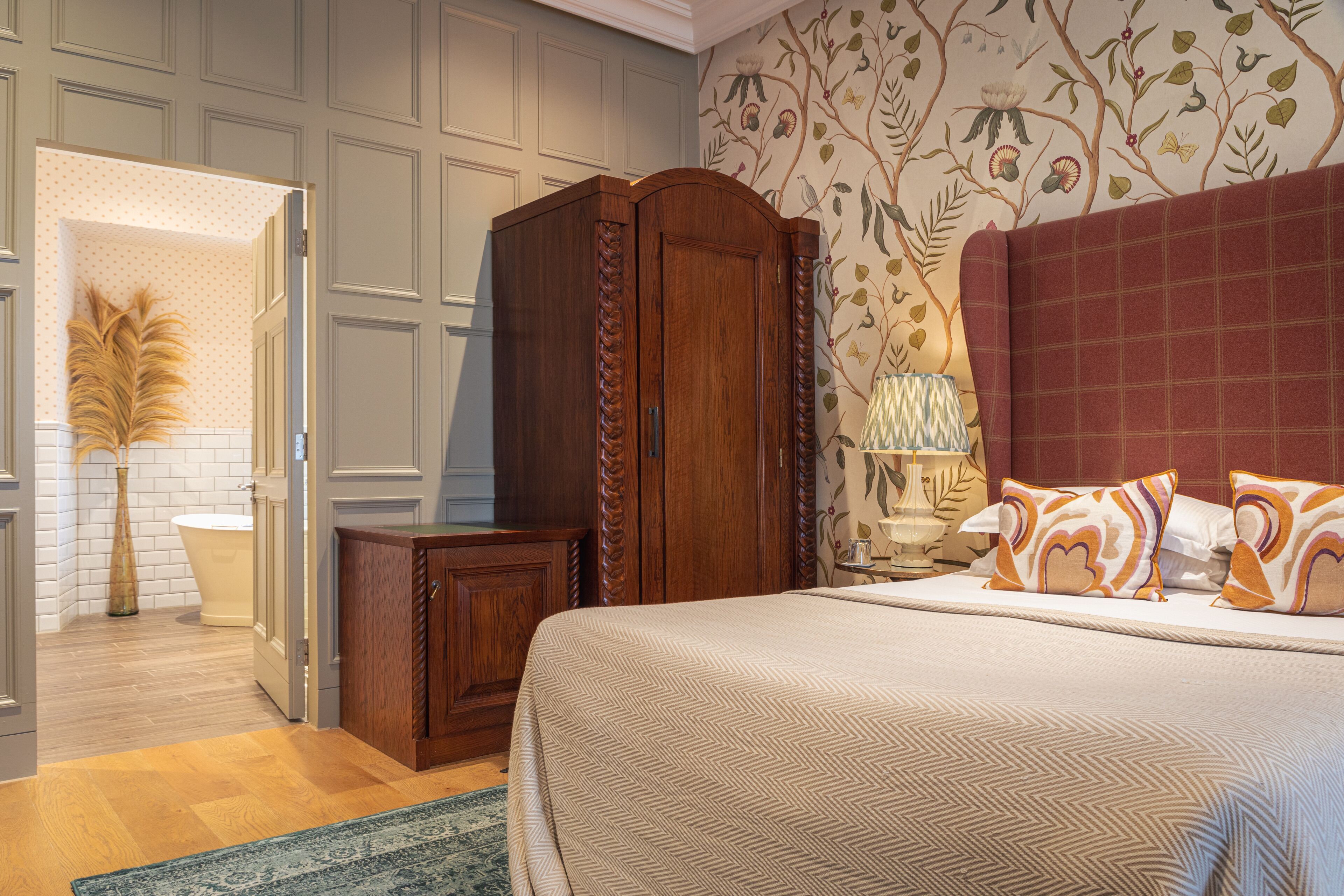 A bedroom with a large bed, a wooden wardrobe, a nightstand, and a floral wallpaper.