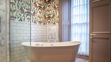 A bathroom with a freestanding bathtub, white tiled walls, and a patterned floral wallpaper.