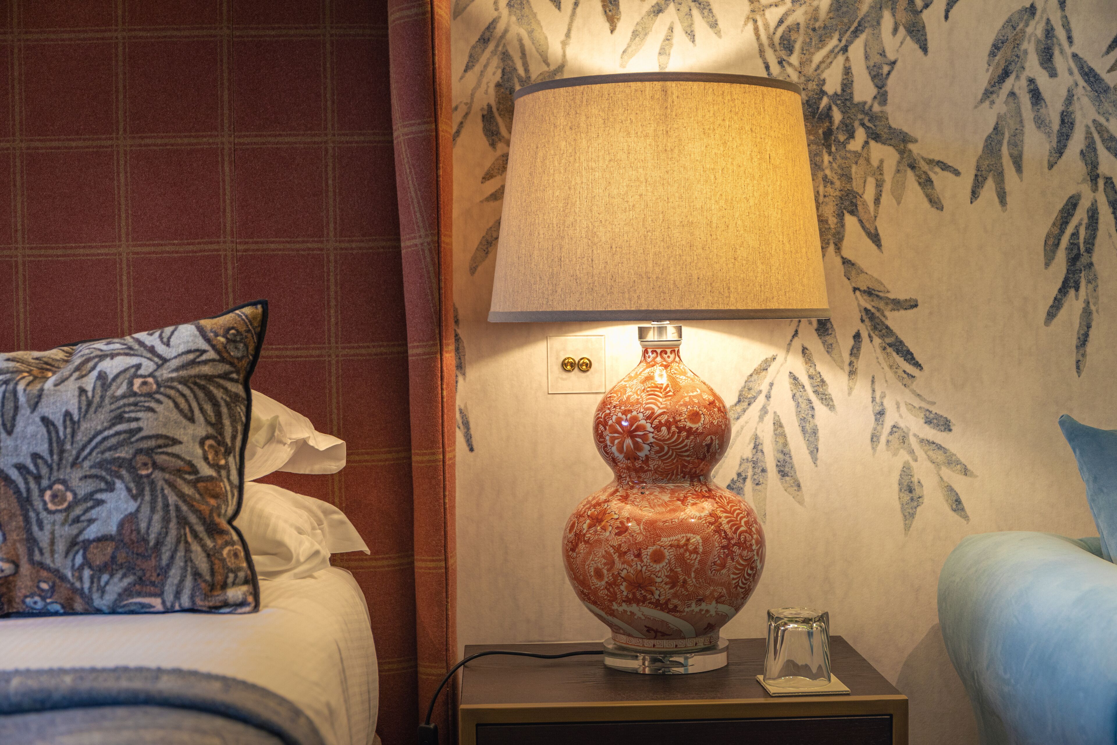 A hotel room with a bed, a nightstand with a lamp, and a wall with a leaf pattern.