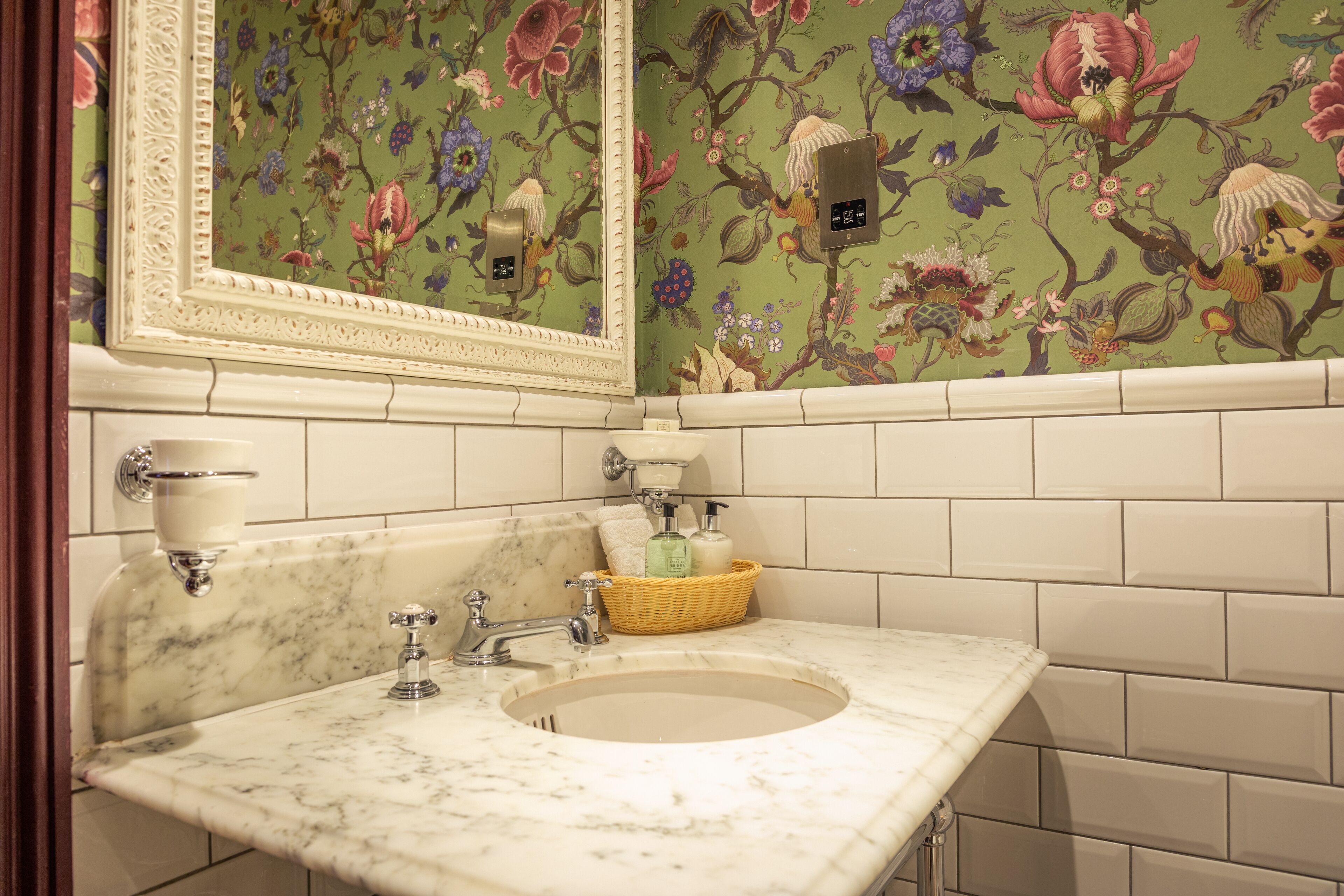 A bathroom with a marble sink, a mirror, and floral wallpaper.