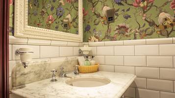 Un baño con lavamanos de mármol, espejo y papel tapiz floral.