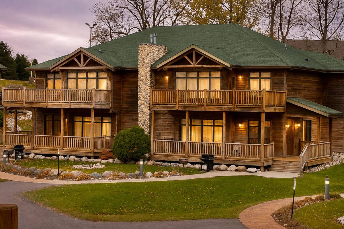 A two-story log cabin with a stone chimney, wooden balconies, and a well-maintained lawn.