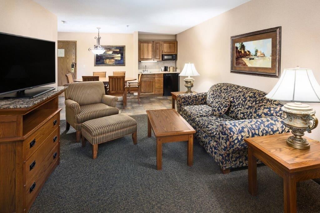 A living room with a sofa, armchair, TV, wooden table, and a lamp.