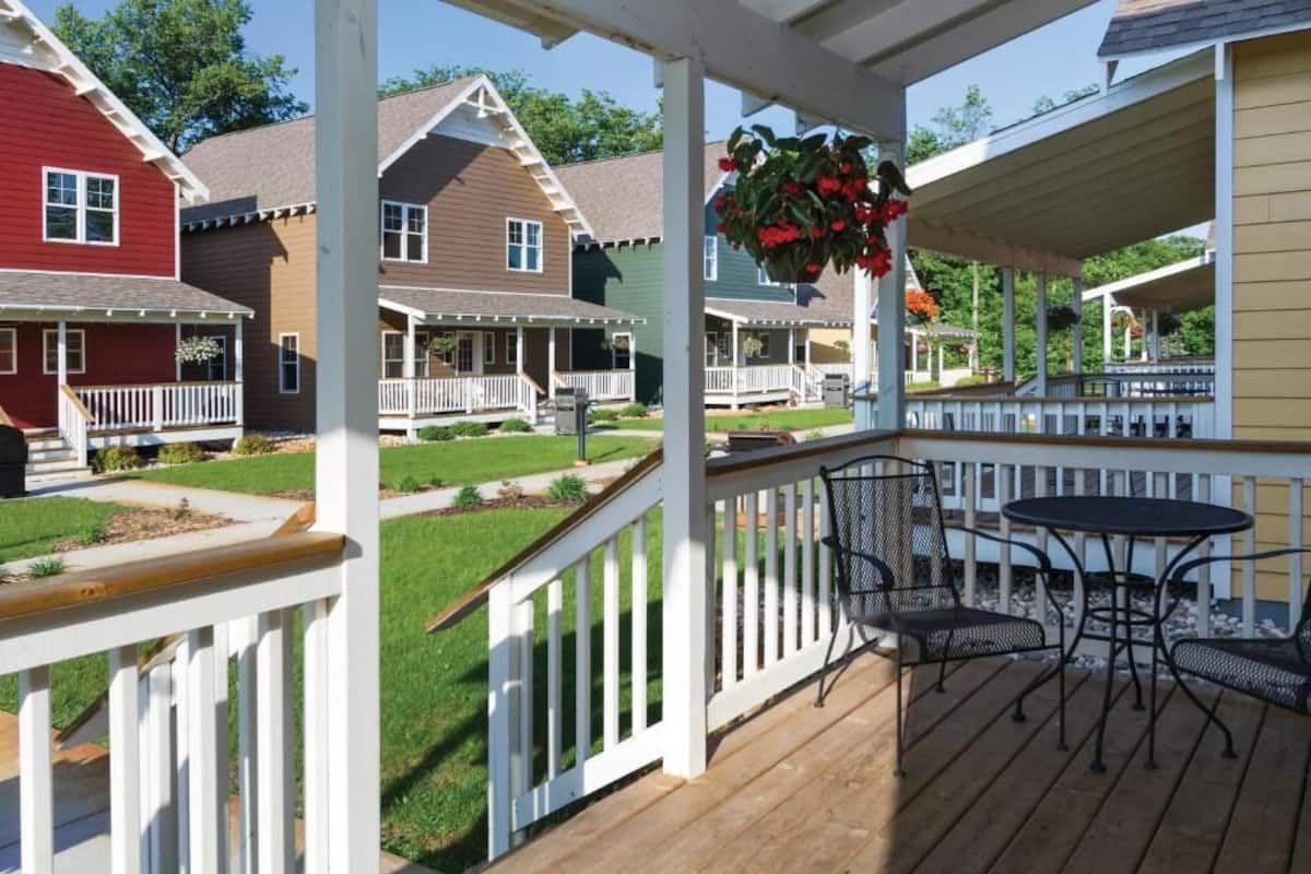 A wooden deck with outdoor furniture, a hanging flower basket, and a view of colorful houses.