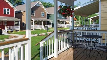 A wooden deck with outdoor furniture, a hanging flower basket, and a view of colorful houses.