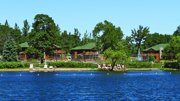 Un chalet au bord du lac, doté de plusieurs cabanes, d’un quai et d’une fontaine.