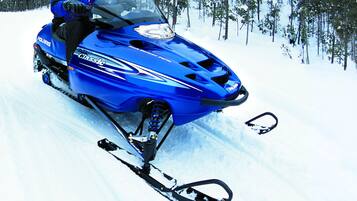 Ein blaues Polaris Schneemobil mit Fahrer in blauer Ausrüstung, das einen verschneiten Pfad durch einen Wald fährt.