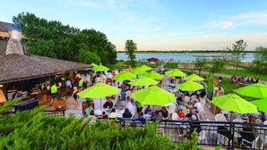 Un espace de restauration en plein air, agrémenté de nombreux parasols verts, de tables et de chaises, et offrant une vue sur une étendue d’eau.