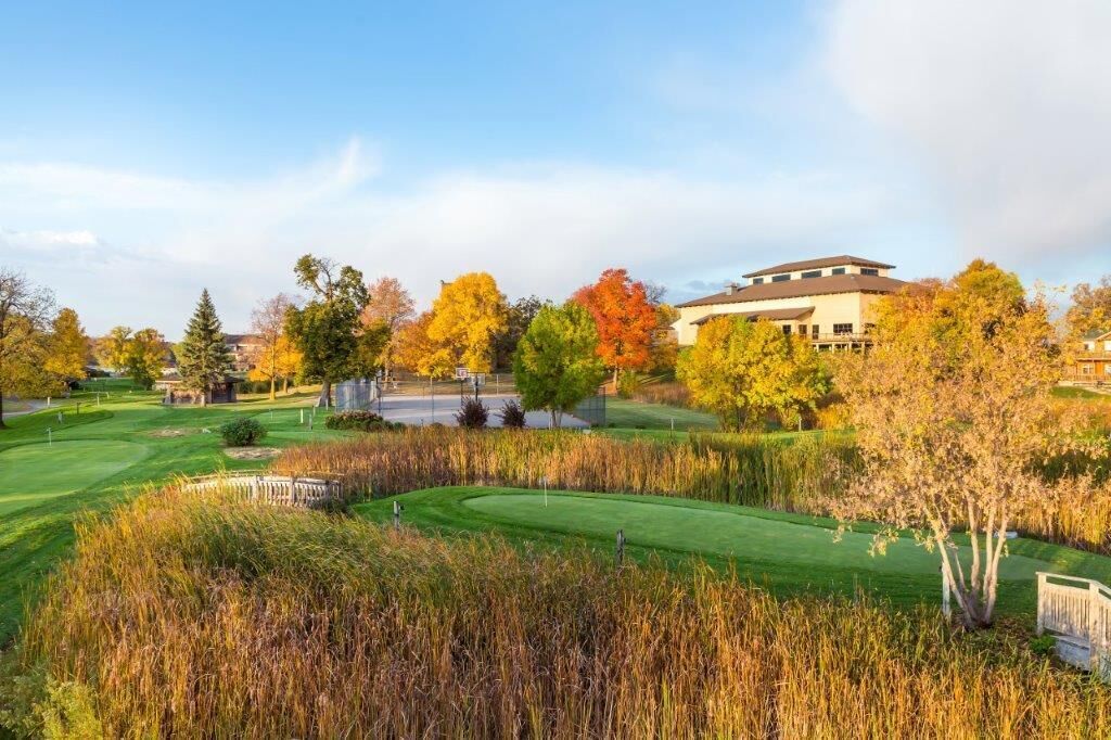 Un parcours de golf doté d’un club-house, entouré d’arbres aux couleurs automnales et surplombé d’un ciel dégagé.