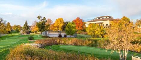 Un parcours de golf doté d’un club-house, entouré d’arbres aux couleurs automnales et surplombé d’un ciel dégagé.