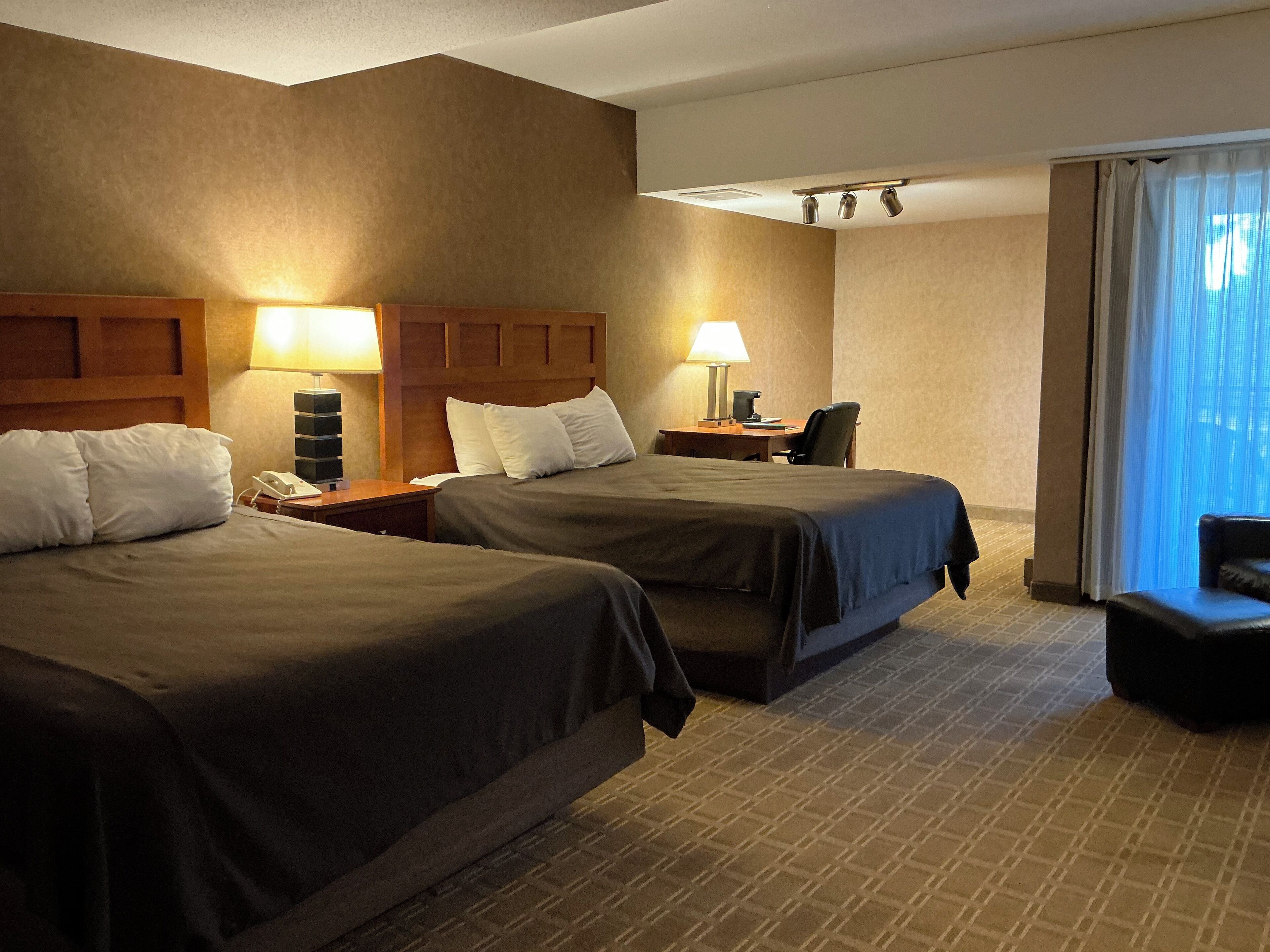 A hotel room with two beds, a desk, a chair, and a window with curtains.
