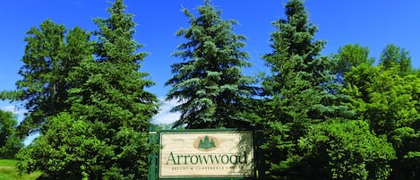 A sign for Arrowwood Resort & Conference Center surrounded by lush greenery and a clear blue sky.