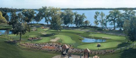 Een golfbaan met een speelveld, een vijver en een meer op de achtergrond.