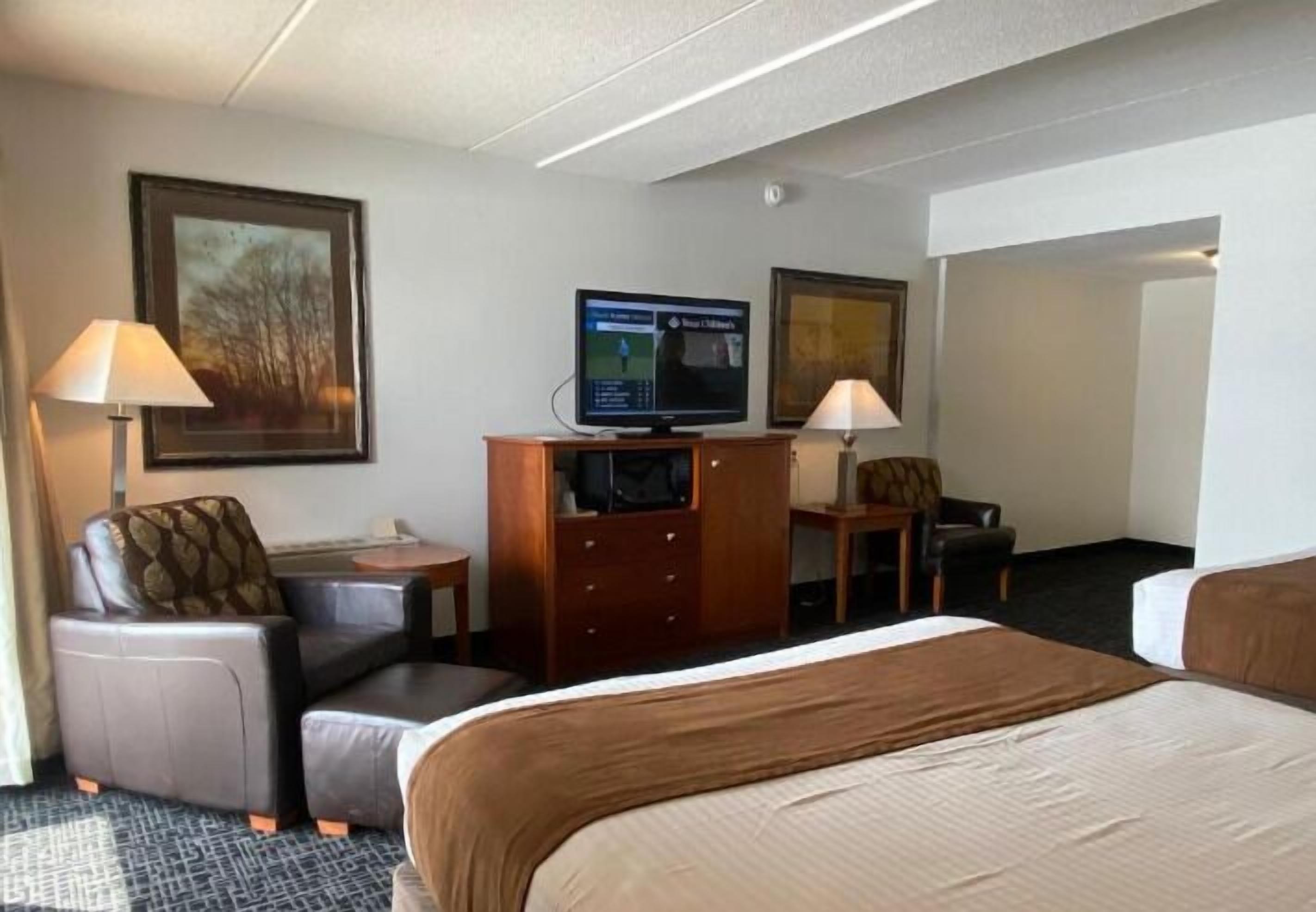 A hotel room with a bed, two chairs, a desk, a television, and two lamps.