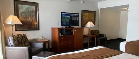 Ein Hotelzimmer mit einem Bett, zwei Sesseln, einem Schreibtisch, einem Fernseher und zwei Lampen.