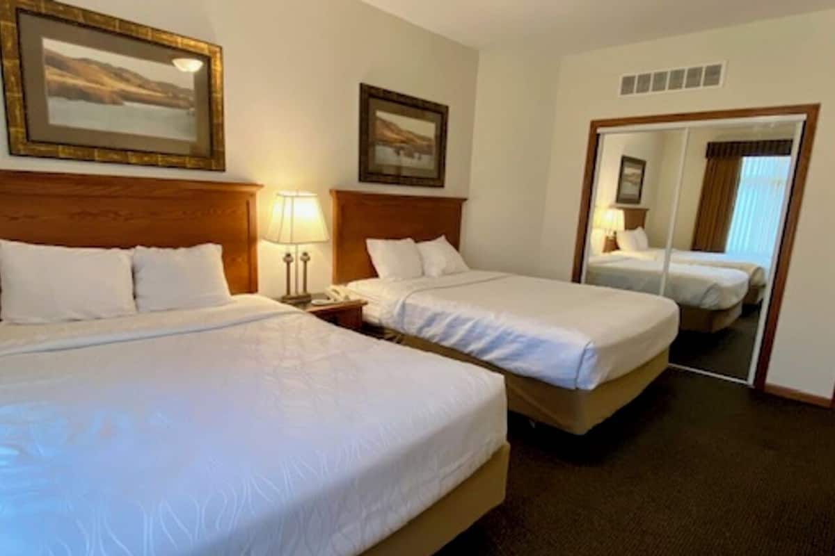 A hotel room with two single beds, a nightstand with a lamp, and a large mirror on the wall.