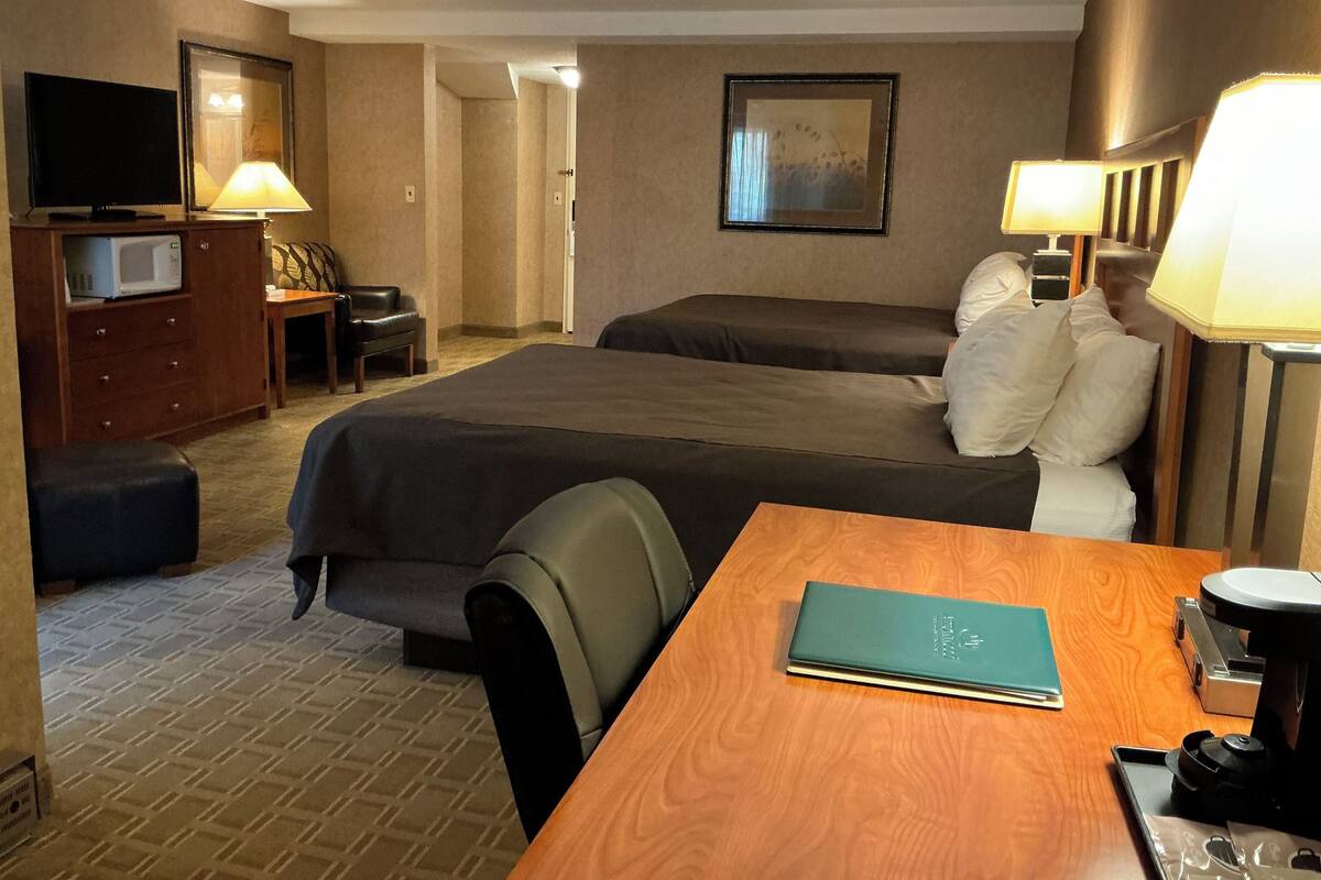 A hotel room with two beds, a desk, a chair, a television, a lamp, and a microwave.