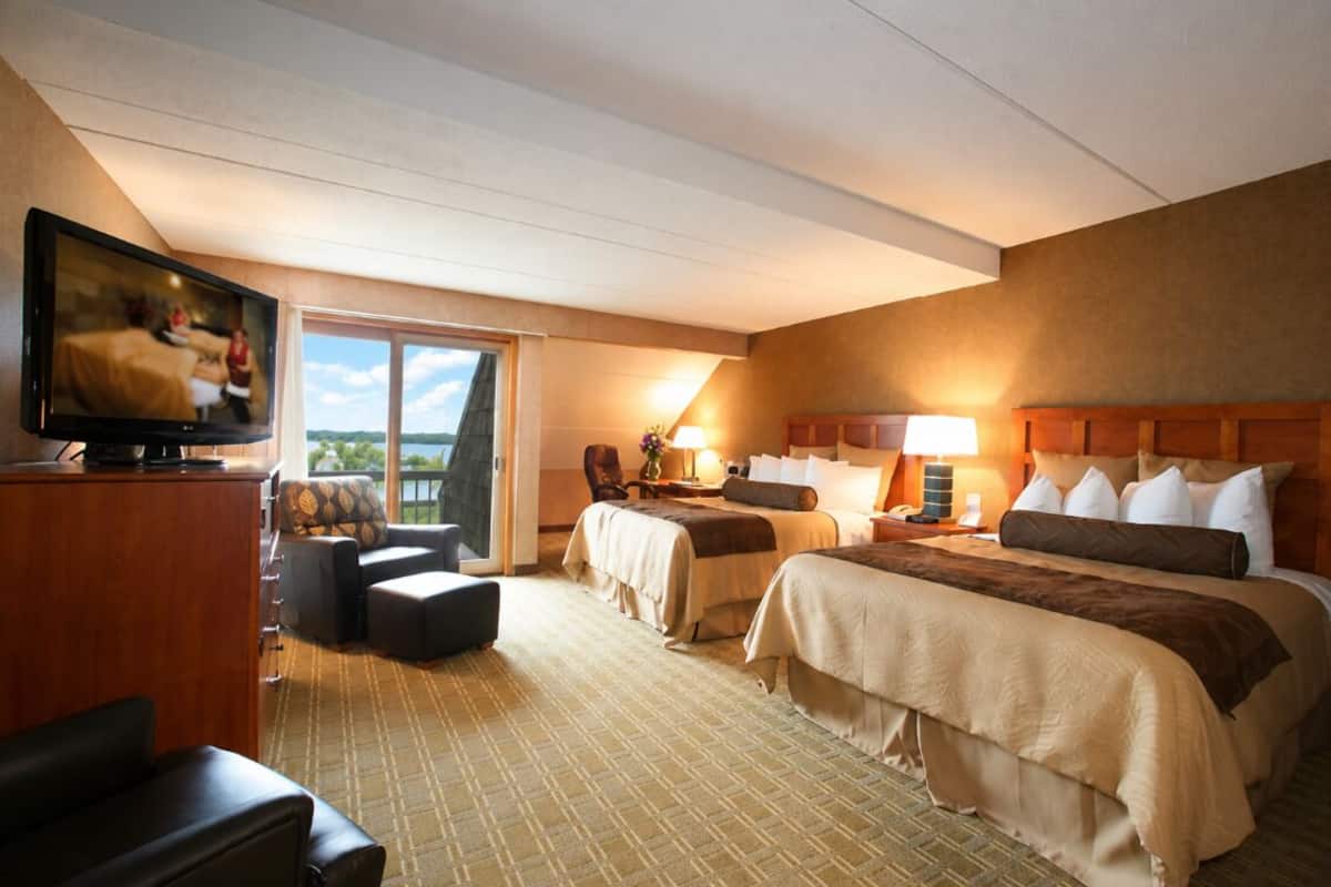 A hotel room with two beds, a TV, a desk, and a view of the outdoors.
