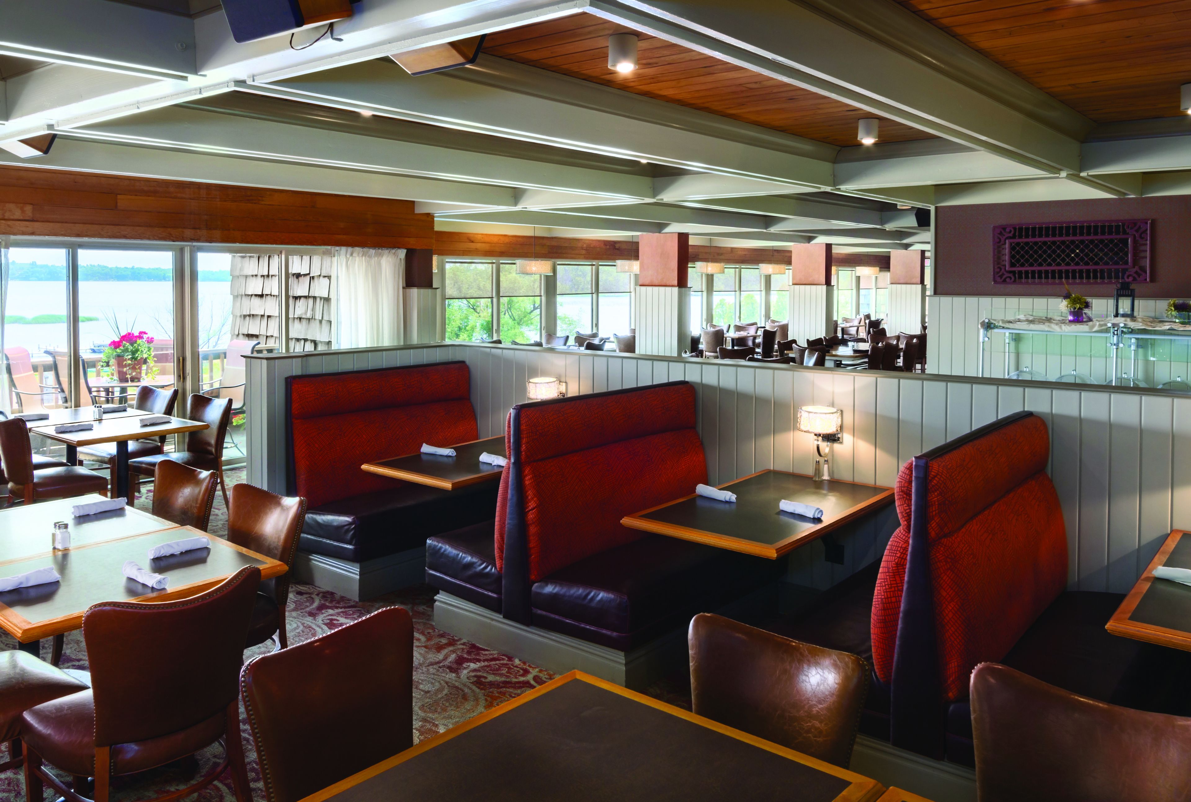 A restaurant with booths and tables, wooden ceiling, large windows, and a view of the outdoors.