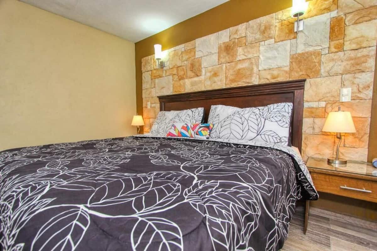 Habitación de hotel con una cama grande, pared de piedra y dos lámparas de noche.