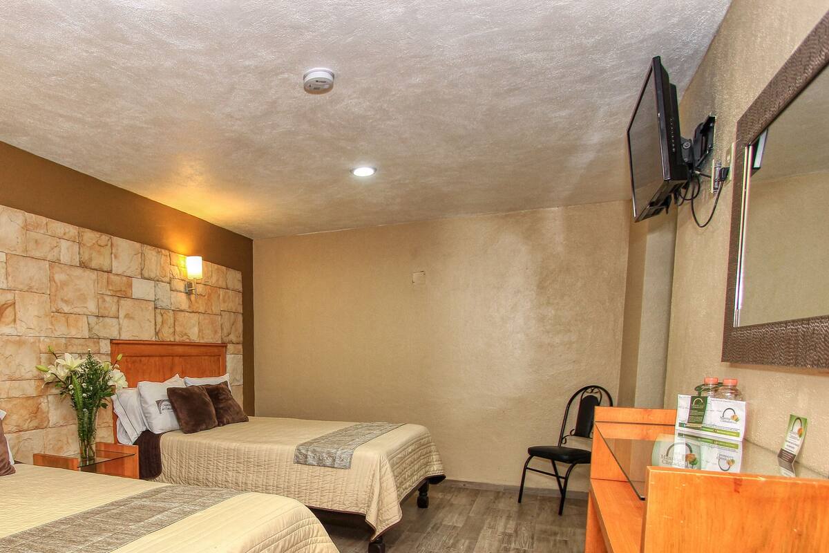 Habitación de hotel con dos camas, un cabecero de madera, una pared de acento de piedra, un escritorio pequeño con una silla y un espejo.
