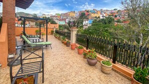 Una terraza con mobiliario exterior, plantas en macetas y vistas a edificios coloridos al fondo.
