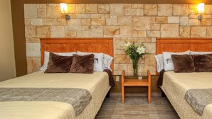 Habitación de hotel con dos camas, una pared de piedra y una mesita de noche de madera con un jarrón de flores.