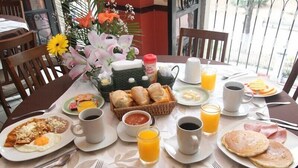 Una mesa de desayuno con diferentes platos, entre ellos huevos, panqueques y fruta.