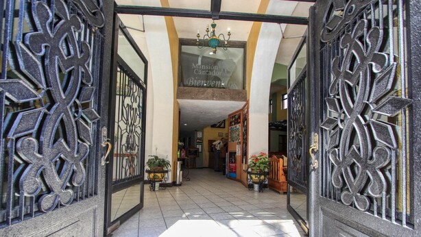 Entrada de hotel con puertas de metal negro ornamentadas, suelo de baldosas y una lámpara de araña.